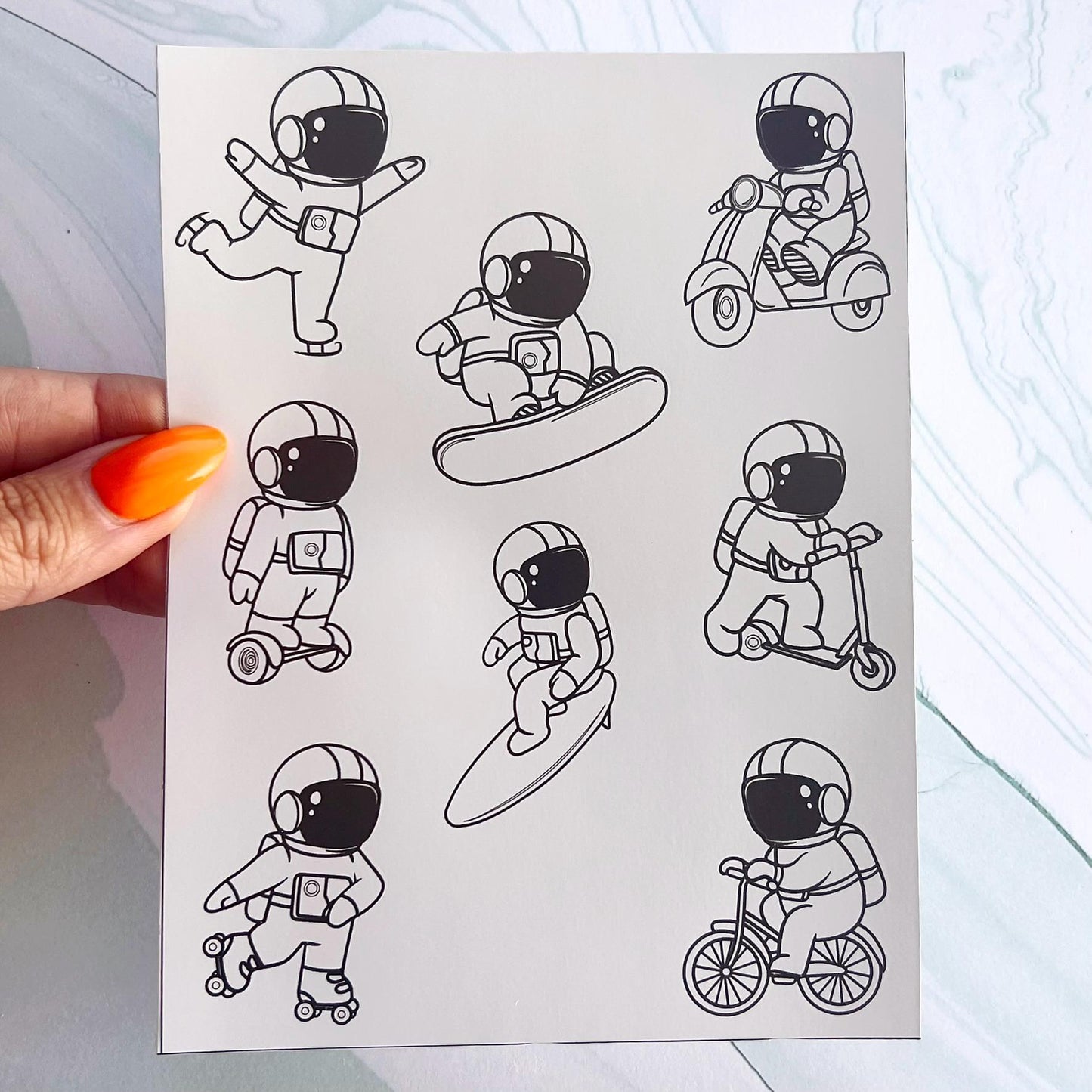 A sheet of black and white stickers featuring astronauts doing different activities. The astronauts are wearing space suits and are riding a scooter, a skateboard, a surfboard, a bicycle, a hoverboard, and a moped.