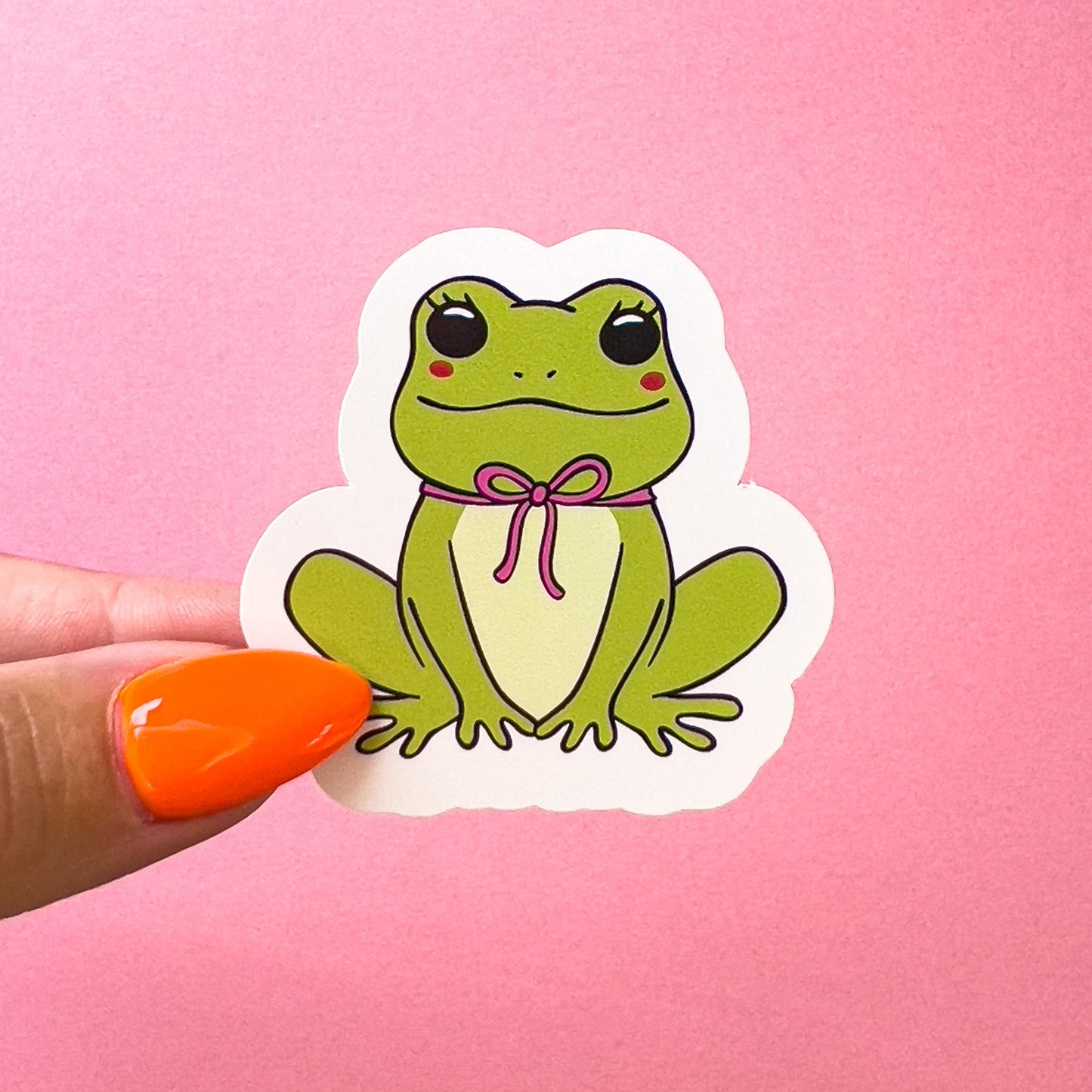 A vinyl decal sticker of a green, cartoon frog with blushed cheeks and a pink bow around its neck. The frog is sitting in a typical frog pose.