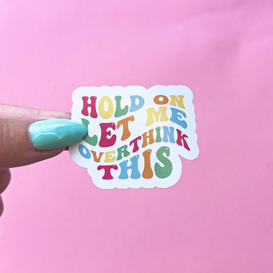 A vinyl decal sticker with the text 'Hold On Let Me Overthink This' in a rainbow of colors. The text is in a retro font style.