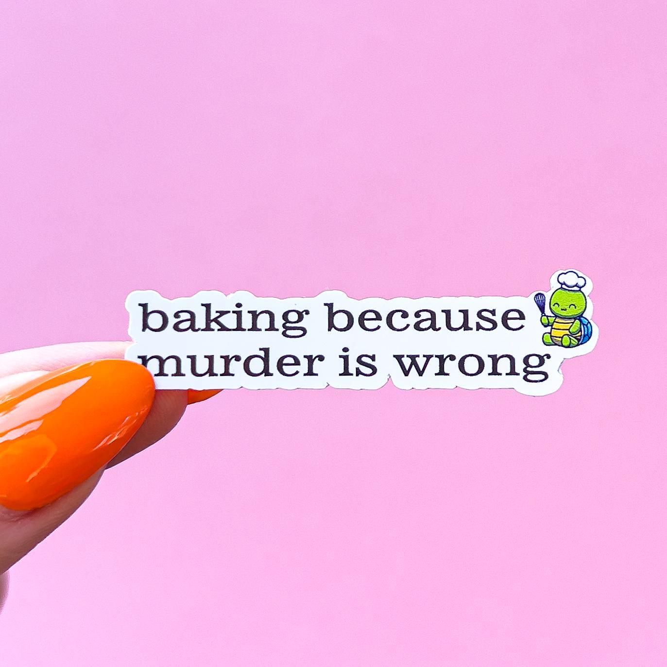 A vinyl decal sticker with black text that reads 'baking because murder is wrong'. A small cartoon turtle wearing a chef's hat and holding a whisk is to the right of the text.