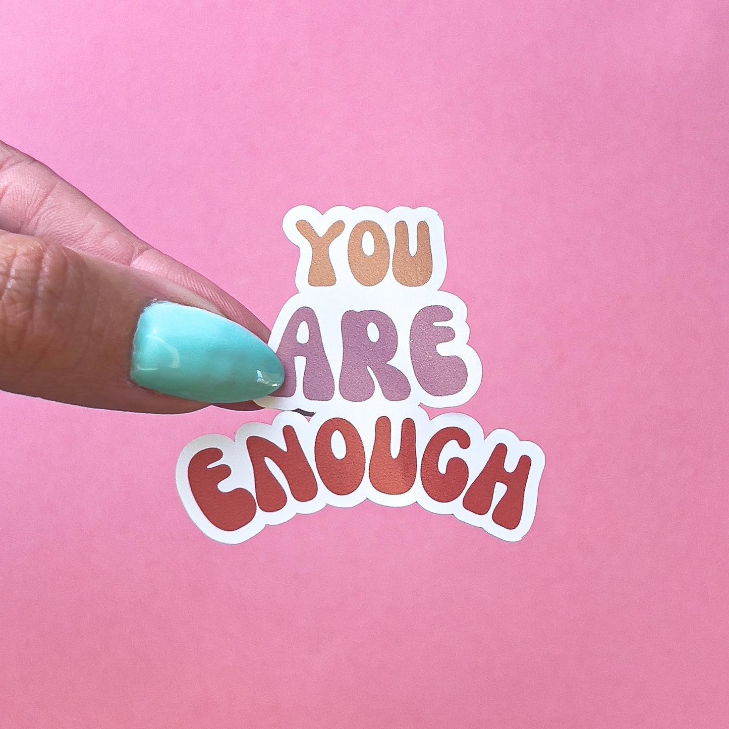 A sticker with the words 'You Are Enough' in a rainbow gradient color scheme. The words are in a stylized font with rounded edges.