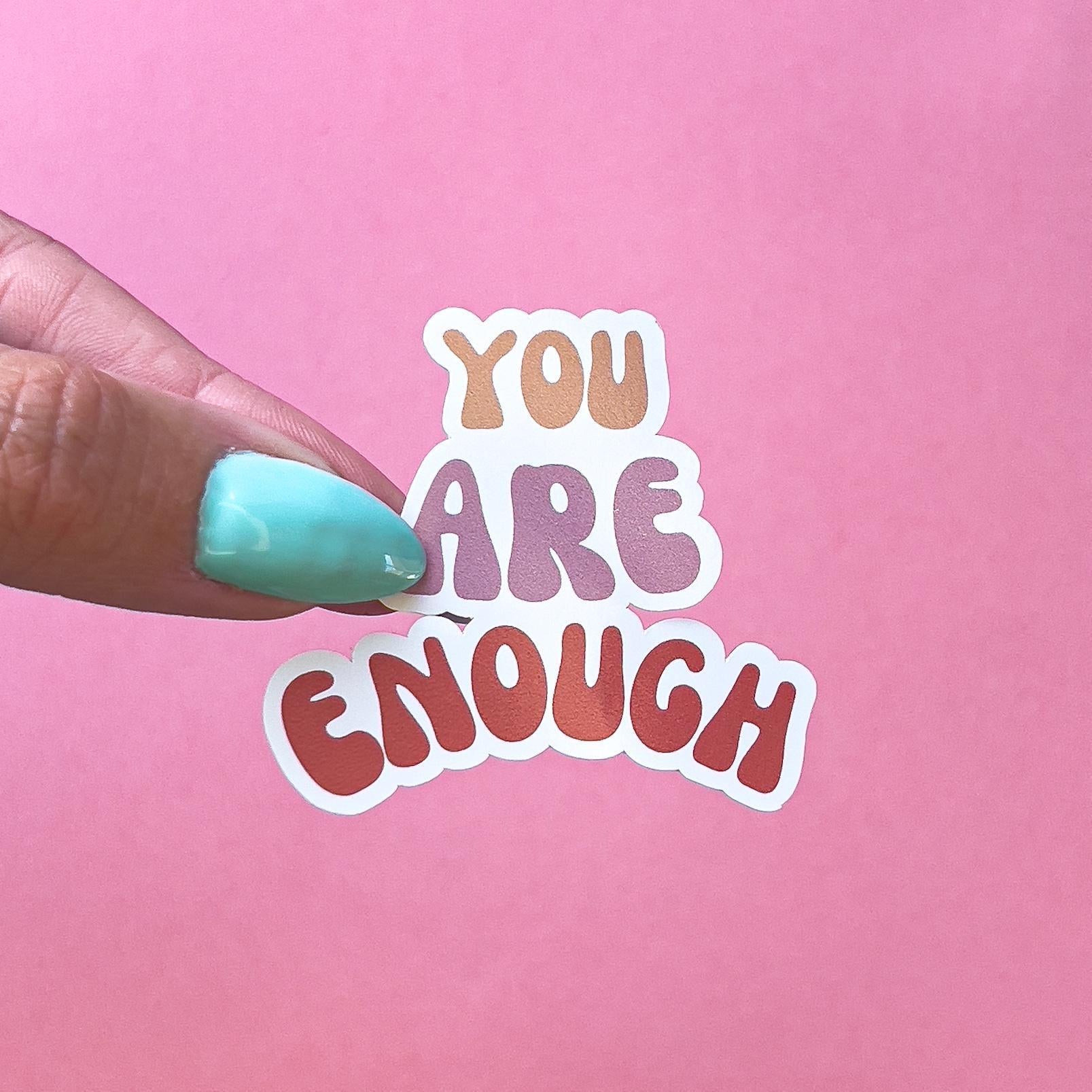 A sticker with the words 'You Are Enough' in a rainbow gradient color scheme. The words are in a stylized font with rounded edges.
