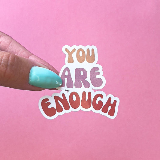 A sticker with the words 'You Are Enough' in a rainbow gradient color scheme. The words are in a stylized font with rounded edges.