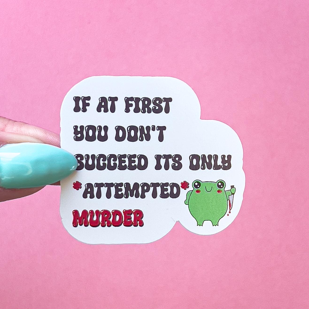 A vinyl decal sticker with the words "IF AT FIRST YOU DONT SUCCEED ITS ONLY *ATTEPMTED* MURDER" in red and black lettering. A smiling, very round, cartoon frog with red blushed cheeks is to the right of the words holding a bloody knife.