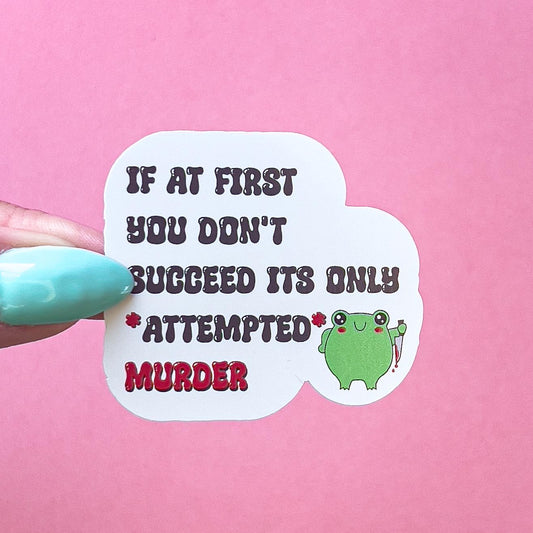 A vinyl decal sticker with the words "IF AT FIRST YOU DONT SUCCEED ITS ONLY *ATTEPMTED* MURDER" in red and black lettering. A smiling, very round, cartoon frog with red blushed cheeks is to the right of the words holding a bloody knife.
