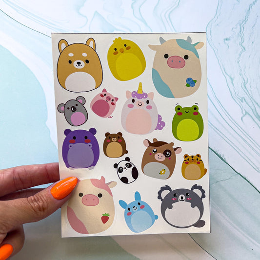 A vinyl sticker sheet featuring round cartoon squishy animals. The animals include three cows, one brown, one blue, and one pink, a bunny, two koalaa, a corgi dog, a frog, a unicorn, a panda, a chick, a pig, and a bear.