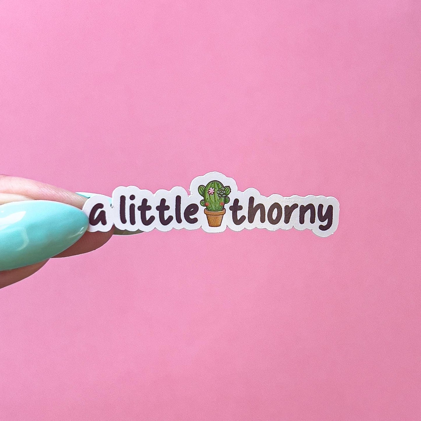 A vinyl decal sticker with black text 'a little thorny', a green, flowering cactus in a brown pot is in between "little" and "thorny".