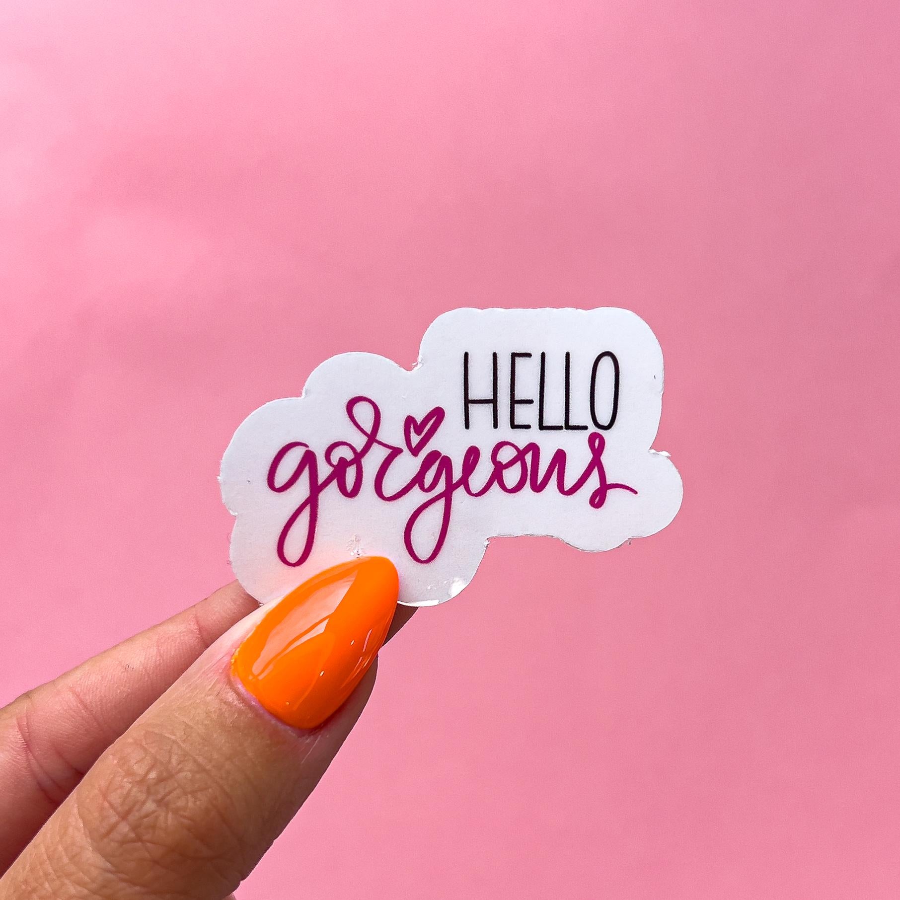 A vinyl decal sticker with a pink heart and the text 'HELLO gorgeous' in black and pink lettering. Printed on clear vinyl.