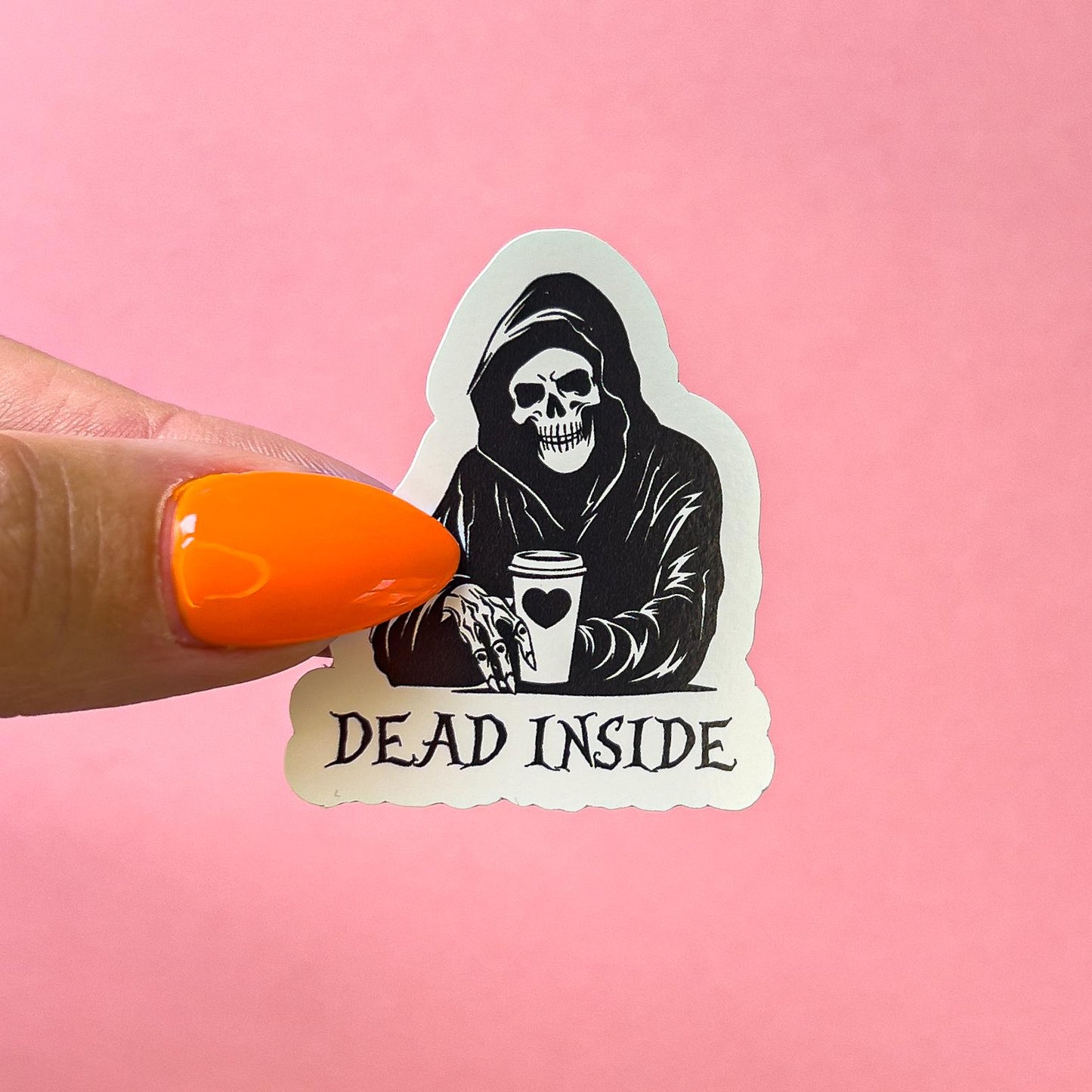 A black and white sticker of a hooded skeleton holding a coffee cup. the coffe cup has a black heart on it.  Black text reads  'DEAD INSIDE' is below the figure.