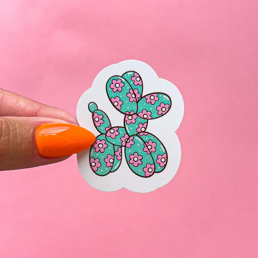 A white sticker with a green and pink balloon dog design. The balloon dog is shaped like a traditional balloon animal and is covered in pink flowers with white centers. The balloon dog is on a white background.