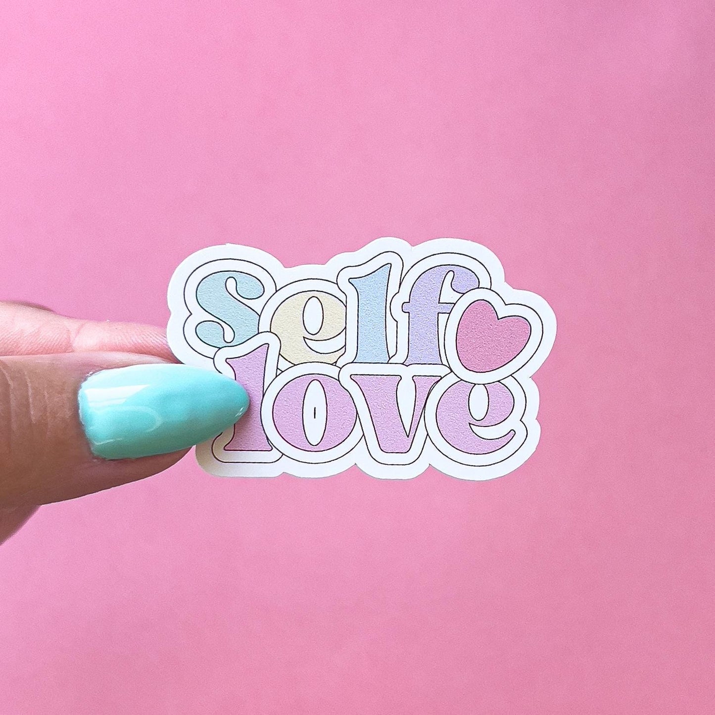 A vinyl decal sticker with the words 'self love' in a pastel color scheme. The letters are outlined in black and there is a small pink heart to the side.