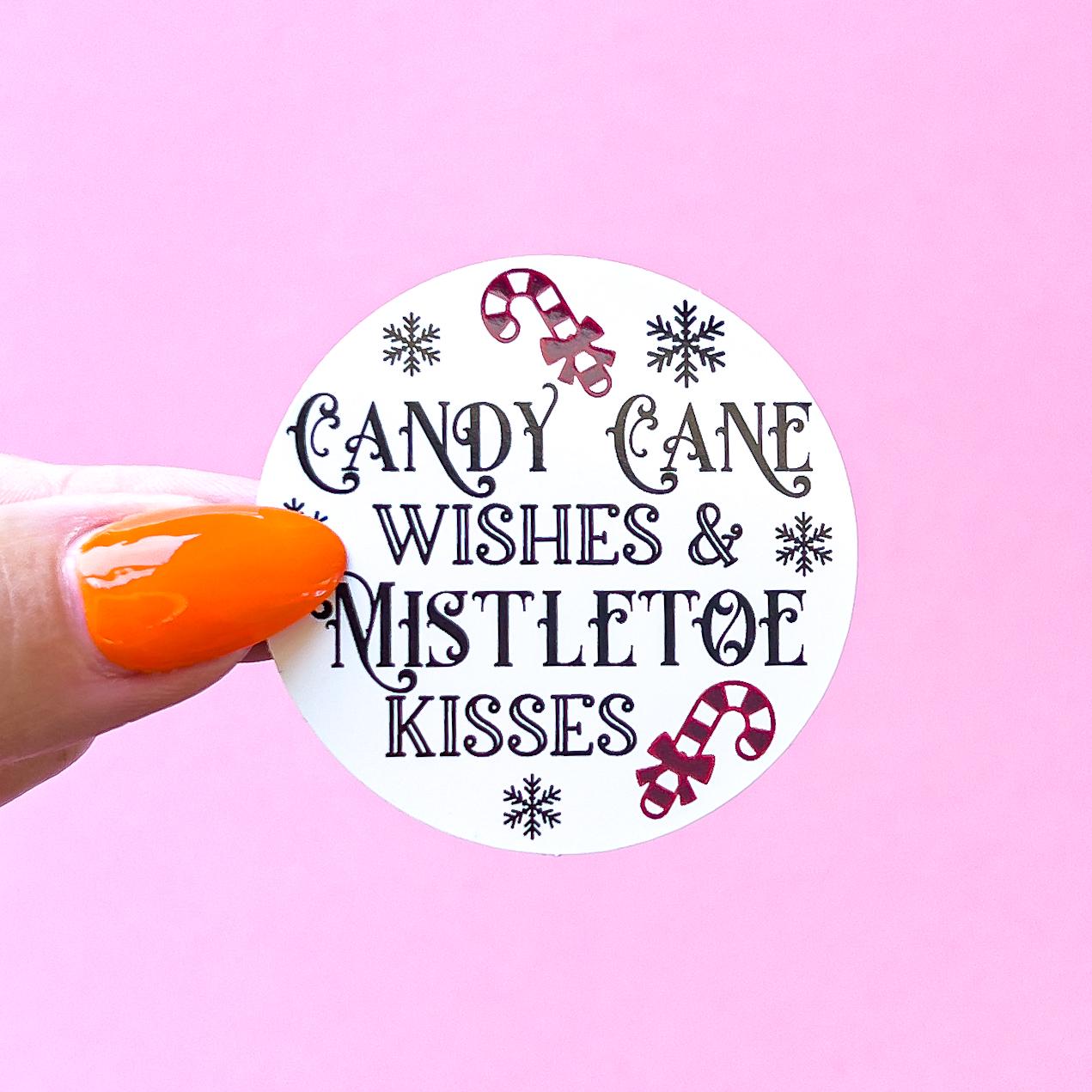 A white round sticker with black text that reads 'Candy Cane Wishes & Mistletoe Kisses'. The sticker has a red and white candy cane design on the top and bottom and snowflakes around the text.