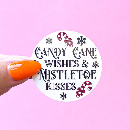 A white round sticker with black text that reads 'Candy Cane Wishes & Mistletoe Kisses'. The sticker has a red and white candy cane design on the top and bottom and snowflakes around the text.