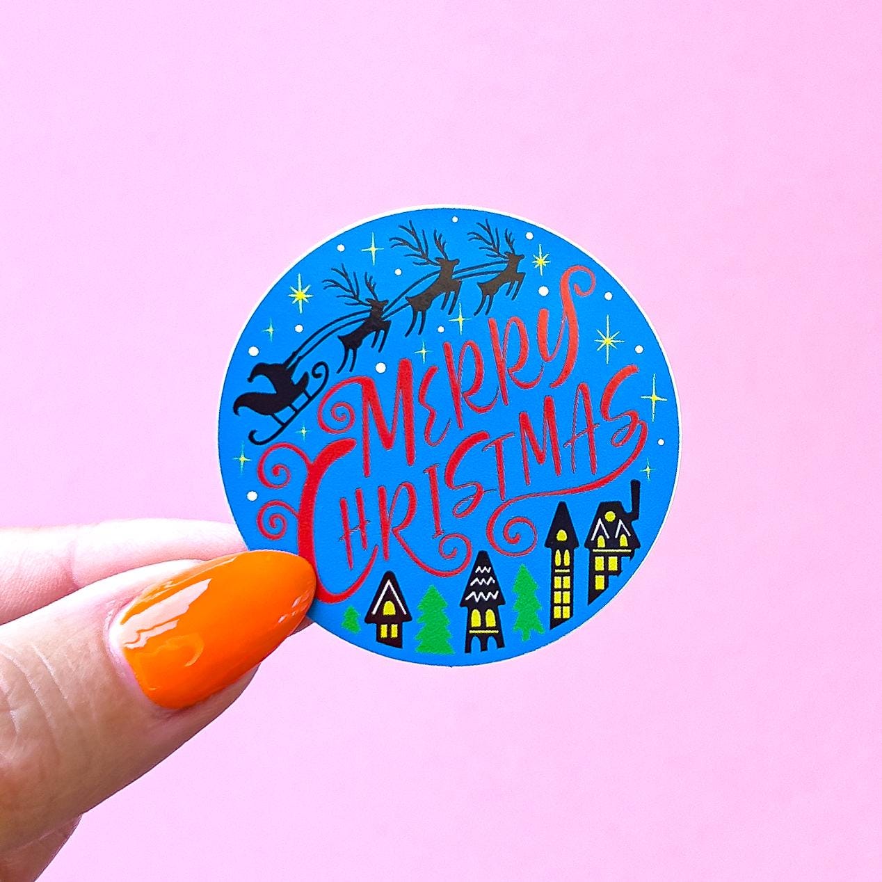 A blue circle sticker with a red 'Merry Christmas' text and a silhouette of Santa Claus in a sleigh pulled by reindeer. The sticker also has a small town scene with houses and trees.