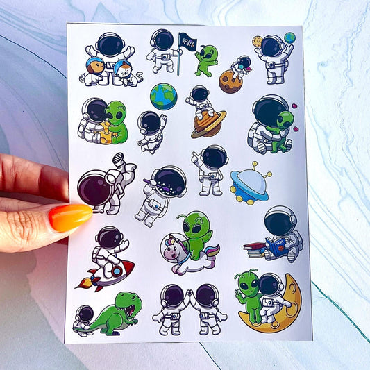 A sheet of colorful stickers featuring various space-themed characters, including astronauts, aliens, a dinosaur, a unicorn, a cat and dog, a Rocketship, a spaceship, and planets. The stickers are perfect for adding a fun and whimsical touch to any project.