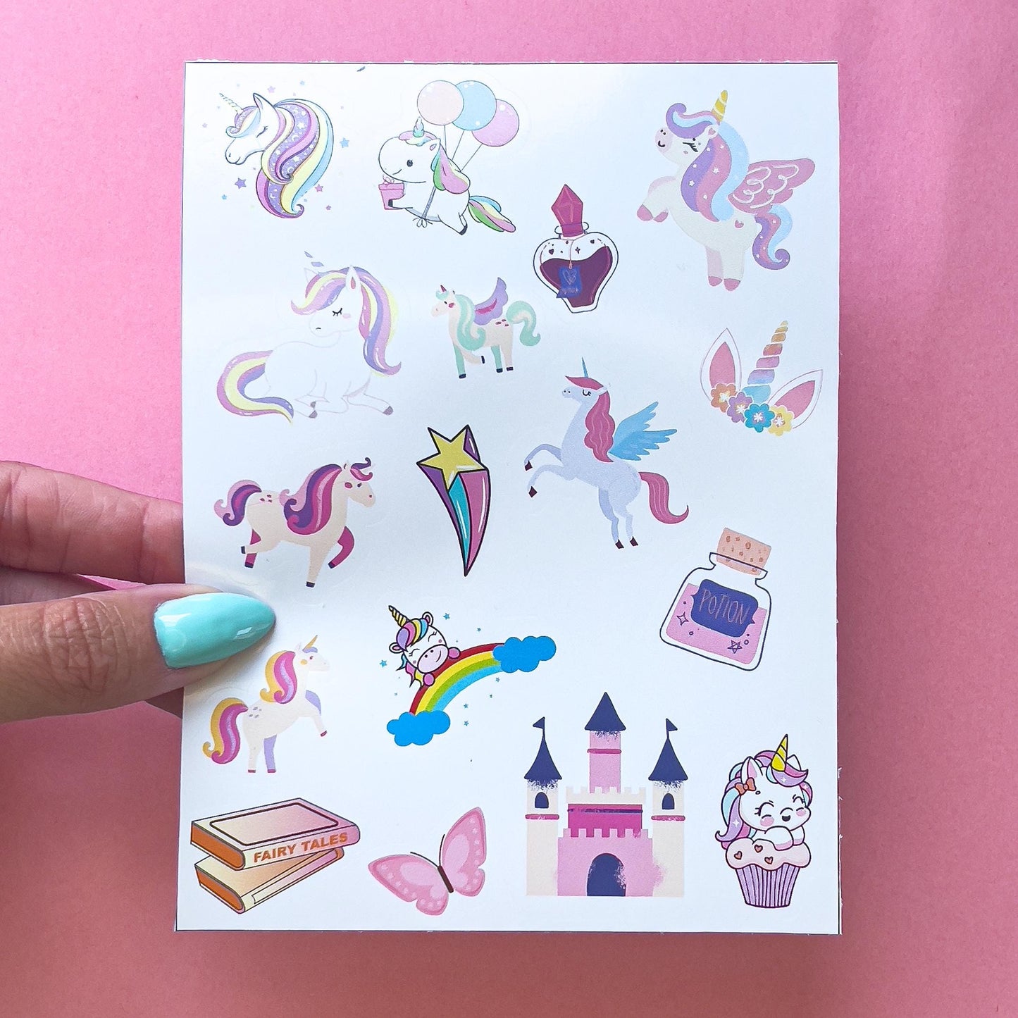 A sheet of unicorn themed stickers. The stickers include unicorns, rainbows, stars, a castle, a potion bottle, and a book that says 'Fairy Tales'. The stickers are on a white background.