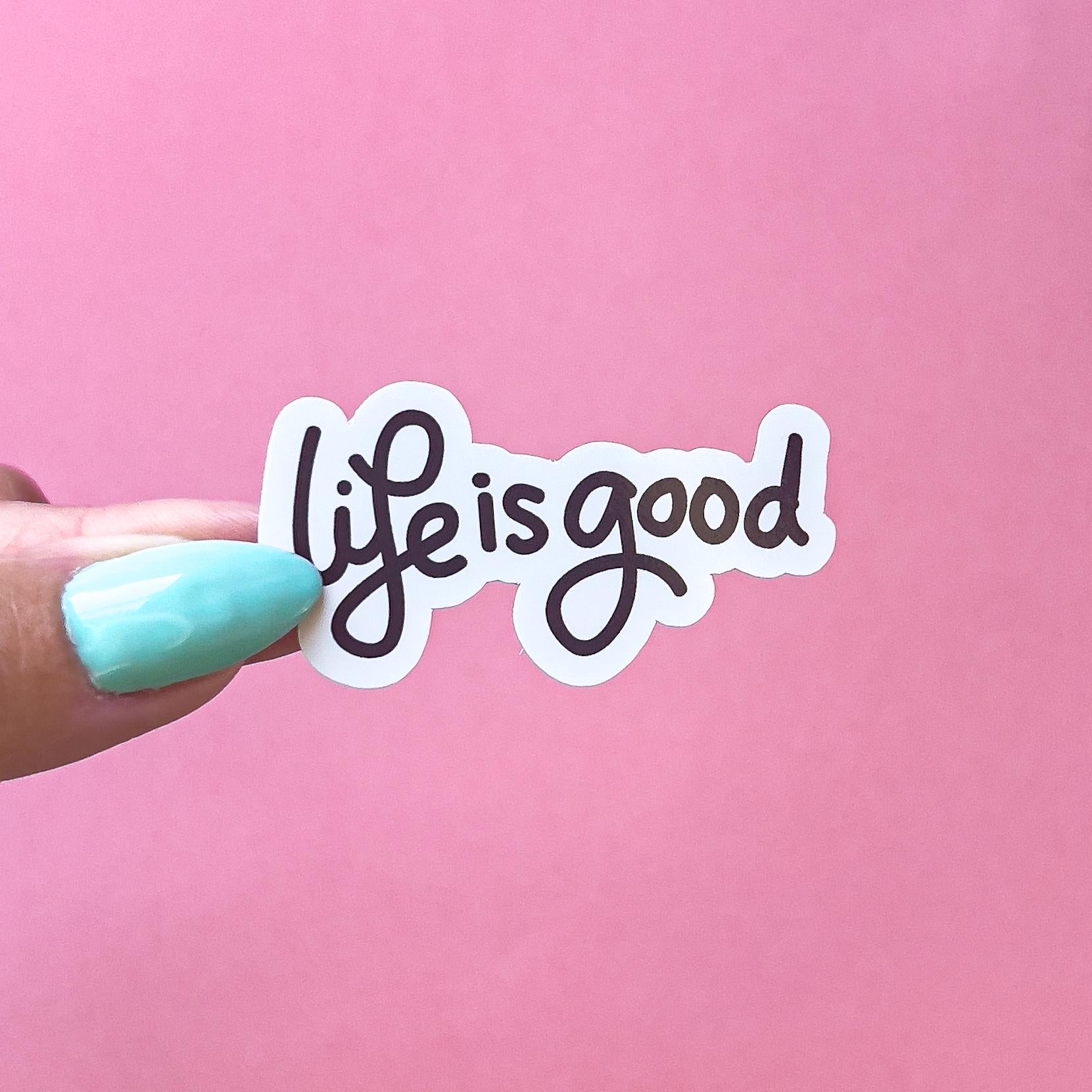 A vinyl decal sticker with black cursive text that reads 'life is good'.