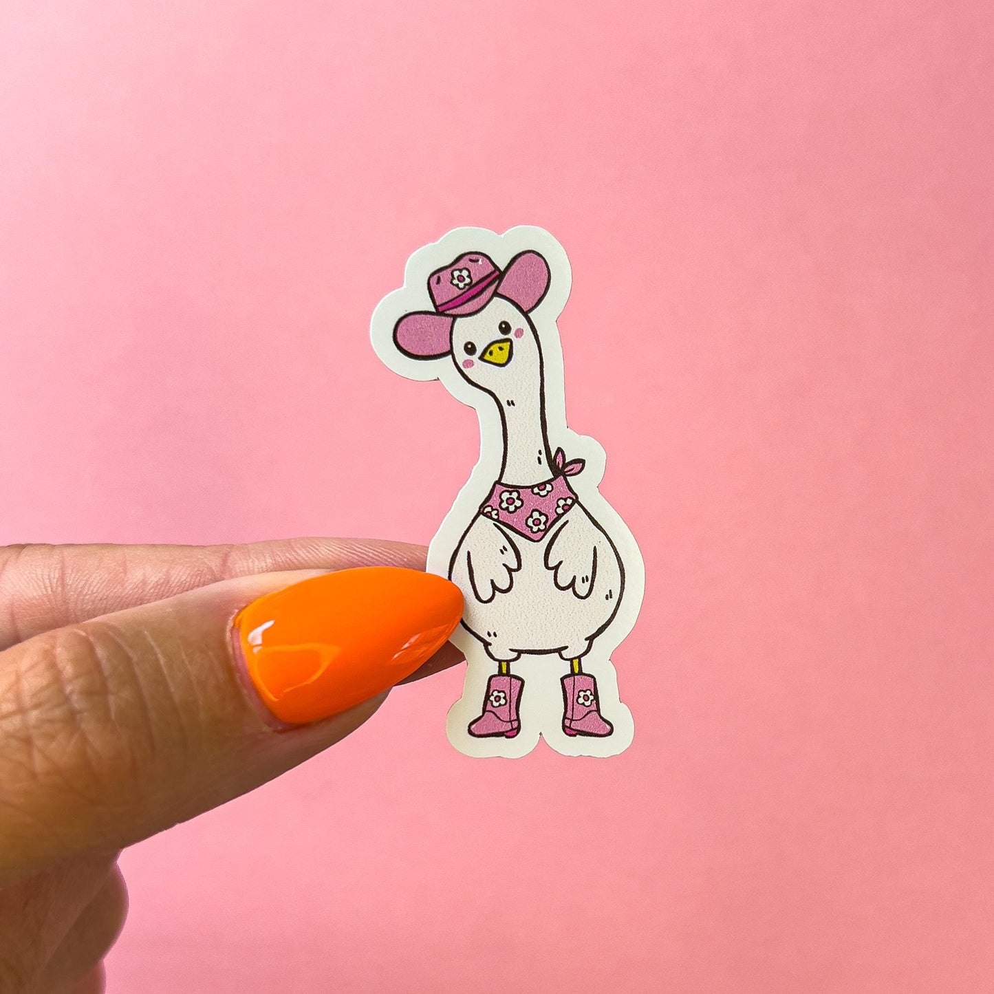 A vinyl decal sticker of a cowboy/western themed goose/duck. The goose/duck is wearing a pink cowboy hat, pink cowboy boots, and a pink bandana with white flowers around its neck. The goose/duck has a yellow beak and is standing, facing forward. It's wings are slightly to the front of its body and its head is tilted to the side. The goose/duck has pink blushed cheeks.