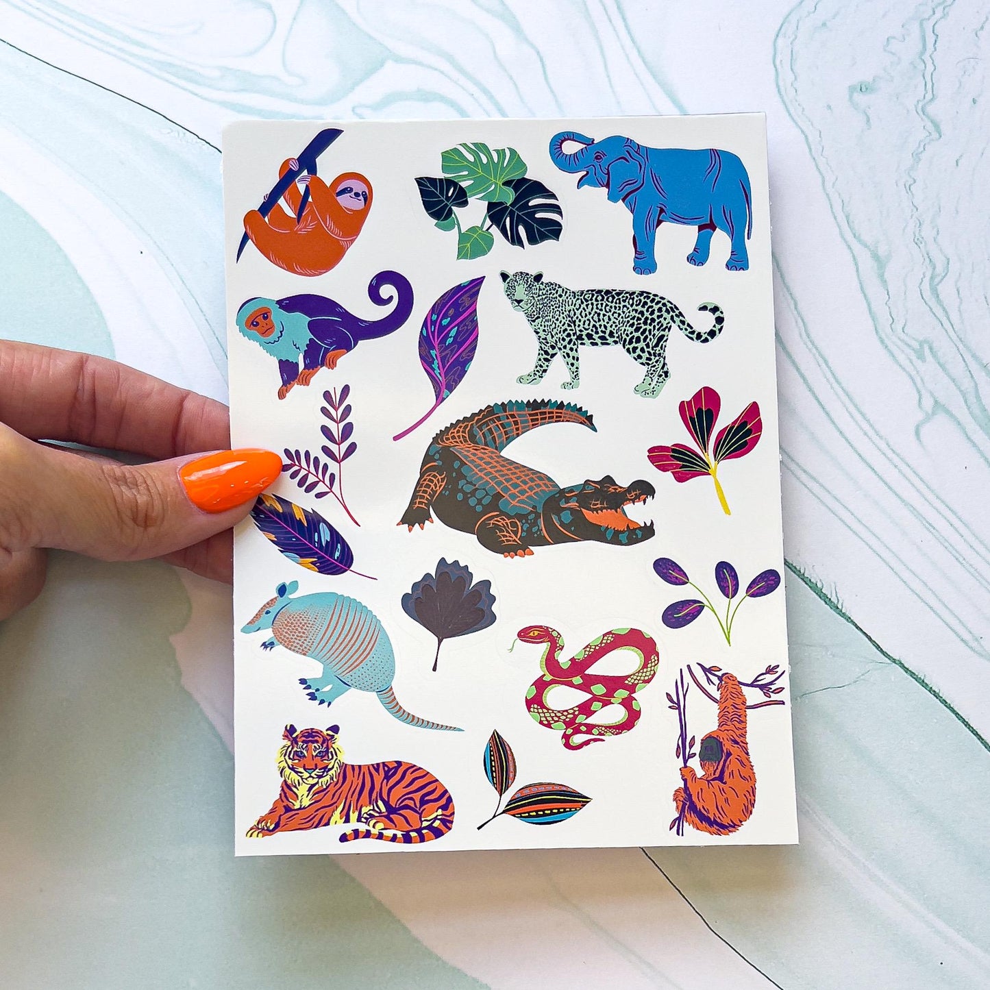 A sheet of various animals and plant stickers. The sticker include sloths, tigers, orangutans, armadillos, elephants, cheetahs, ect in bright unrealistic colors. The colors include bright orange, purple, green, mint, purple, yellow, purple, ect.