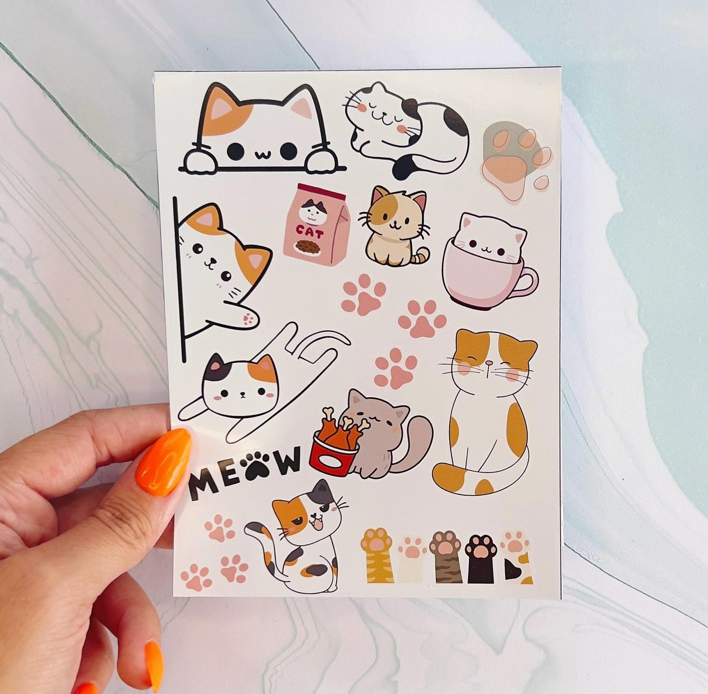 A vinyl sticker sheet featuring cartoon cats, paw prints, cat paws, and the word meow. The cats are in various poses and colors including: white, black, orange, grey, and brown. The paw prints are light pink. The word "MEOW" is black and the "O" is a paw print.