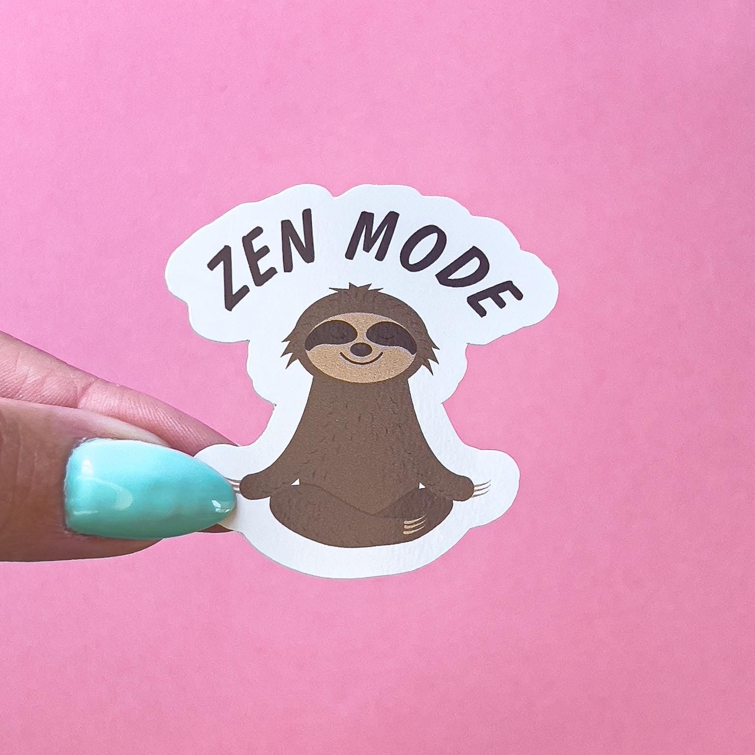 A vinyl decal sticker of a brown and beige sloth  doing the Sukhasana, yoga pose. Above the sloth black text reads “Zen Mode”