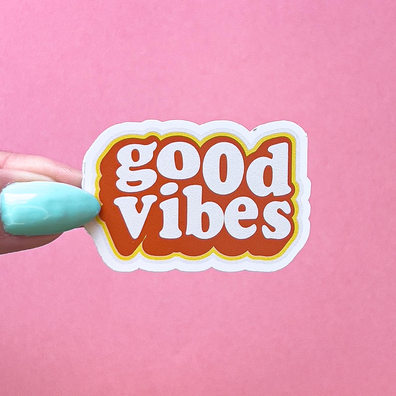A vinyl decal sticker that says 'good vibes' in retro font. The letters are white and outlined in orange and yellow.