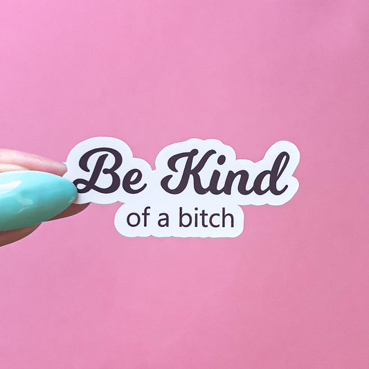 A vinyl decal sticker with black text that reads "Be Kind" in large cursive text. Underneath small, black text reads "of a bitch"