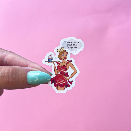 A vinyl decal sticker of a vintage pinup woman wearing a red and white polka dot dress and a chef's hat. She is holding a tray with a cupcake on it. The text in the speech bubble says 'I made you a shut the fucupcake.'