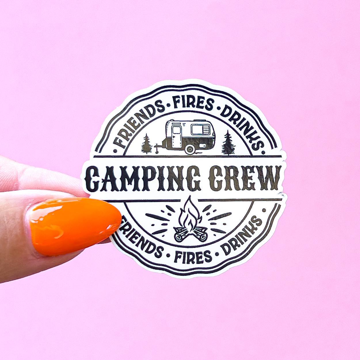 A round sticker with black text and a small camper illustration. The text reads 'Friends Fires Drinks Camping Crew Friends Fires Drinks.'  Two wavy, black lines border the sticker.