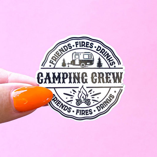 A round sticker with black text and a small camper illustration. The text reads 'Friends Fires Drinks Camping Crew Friends Fires Drinks.'  Two wavy, black lines border the sticker.