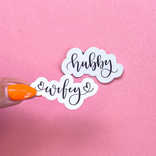 Two vinyl decal sticker of a cursive text that reads "wifey" and "hubby". A heart is on either side of "wifey".