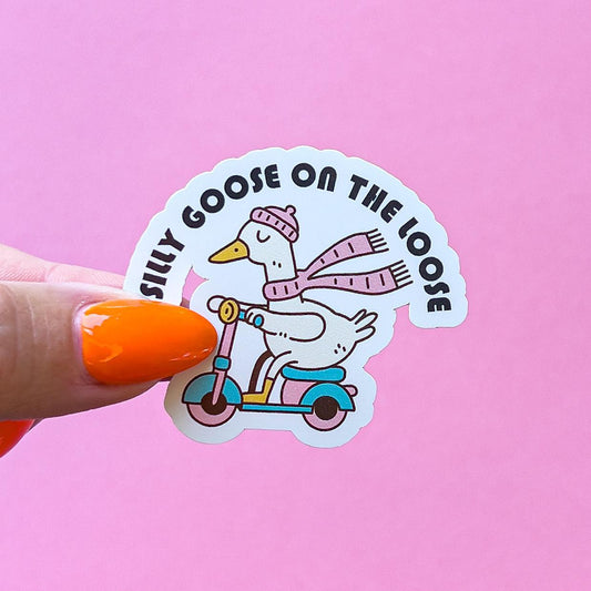 A vinyl decal sticker of a goose wearing a pink hat and scarf riding a blue and pink scooter. The text on the sticker reads 'Silly Goose on the Loose'.