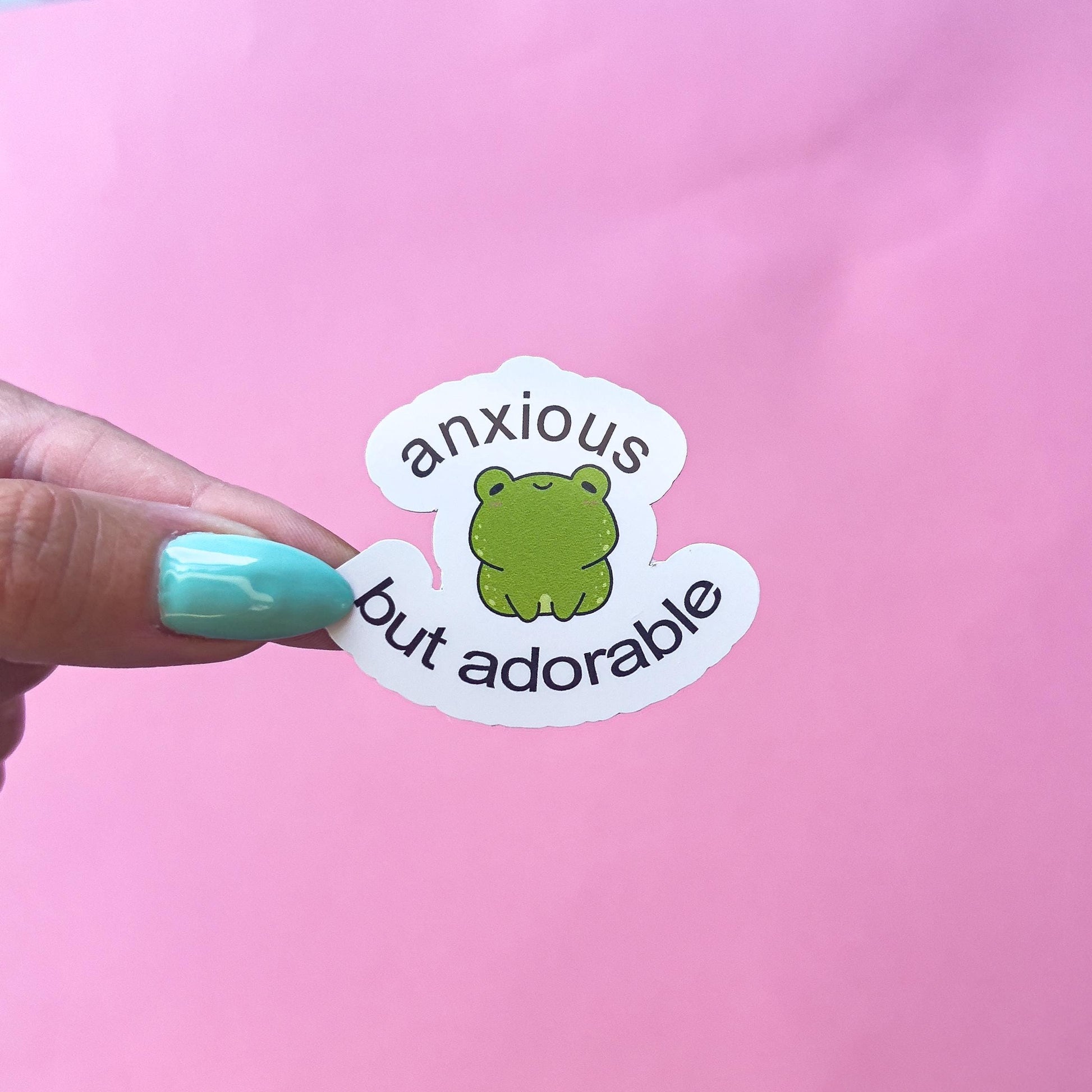 A vinyl decal sticker of a green cartoon kawaii frog with the text 'anxious but adorable'.