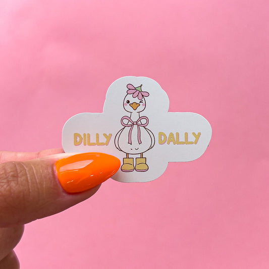 A vinyl decal sticker of a white, cartoon goose/duck wearing a pink flower as a hat, a pink bow, and yellow rain boots. The goose is winking with pink blushed cheeks. The text says 'DILLY DALLY' in yellow letters.