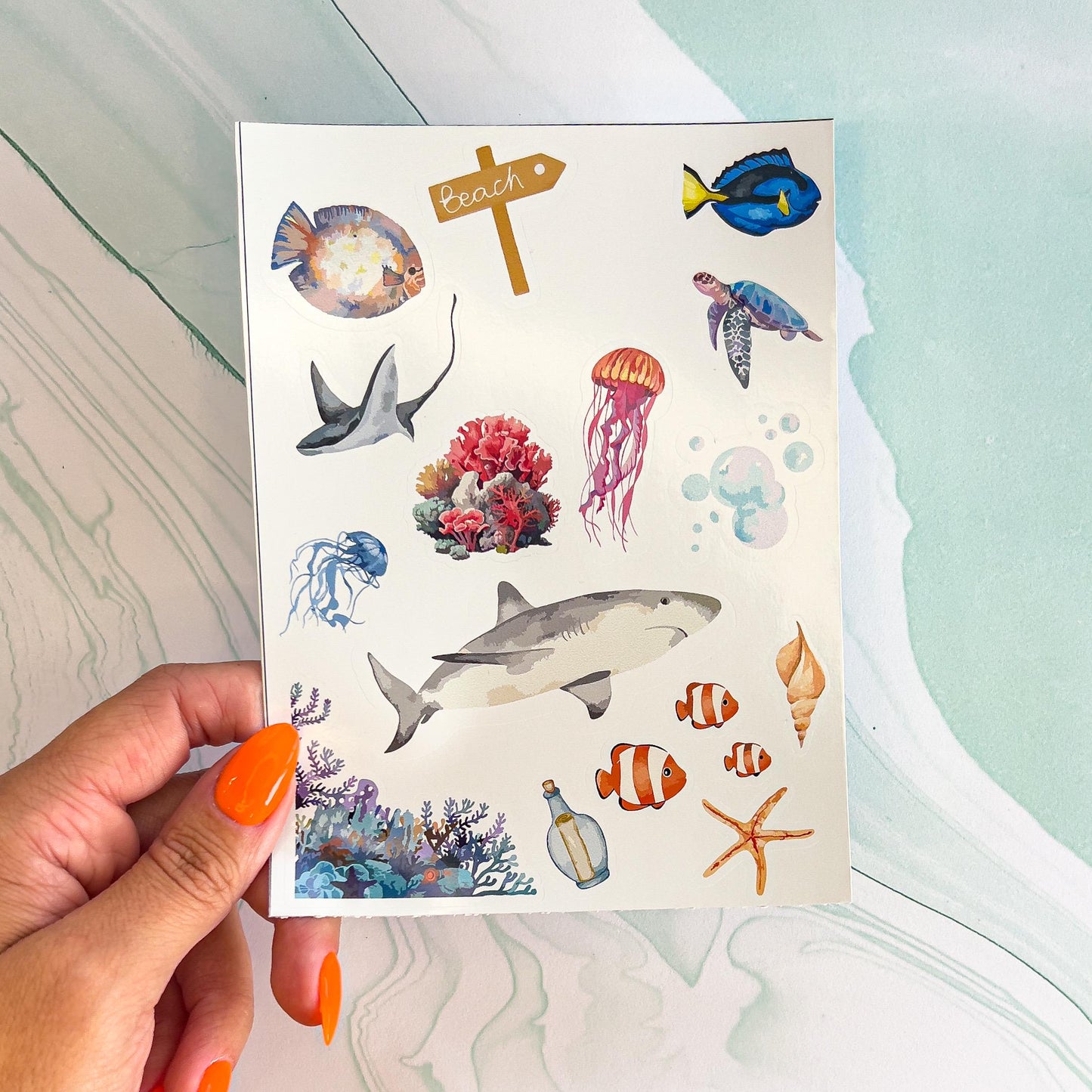 A sheet of underwater/sea life themes stickers. The stickers are in a painted style and include a coral reef, a shark, clown fish, starfish, jellyfish, sea turtle, fish, a sting ray, letter in a bottle, and bubbles.
