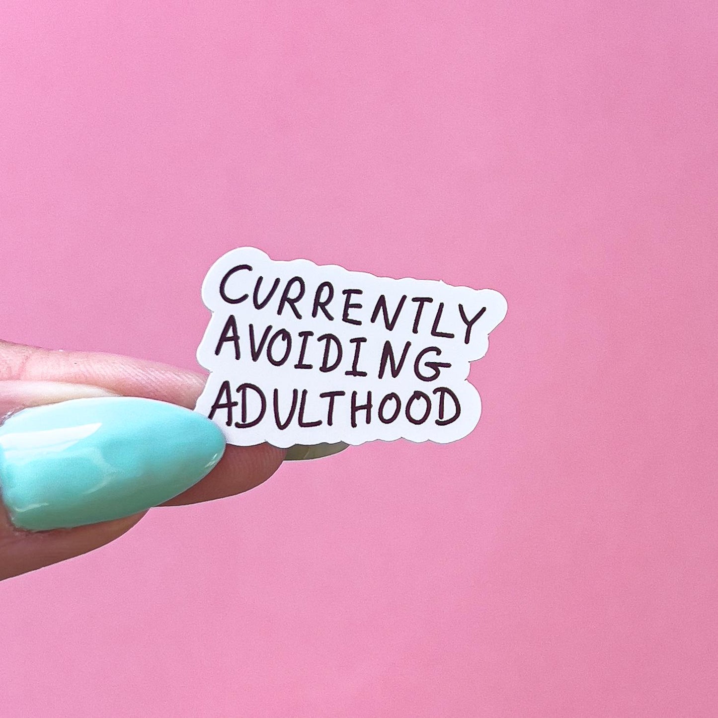 A vinyl decal sticker with black text that reads 'Currently Avoiding Adulthood'.