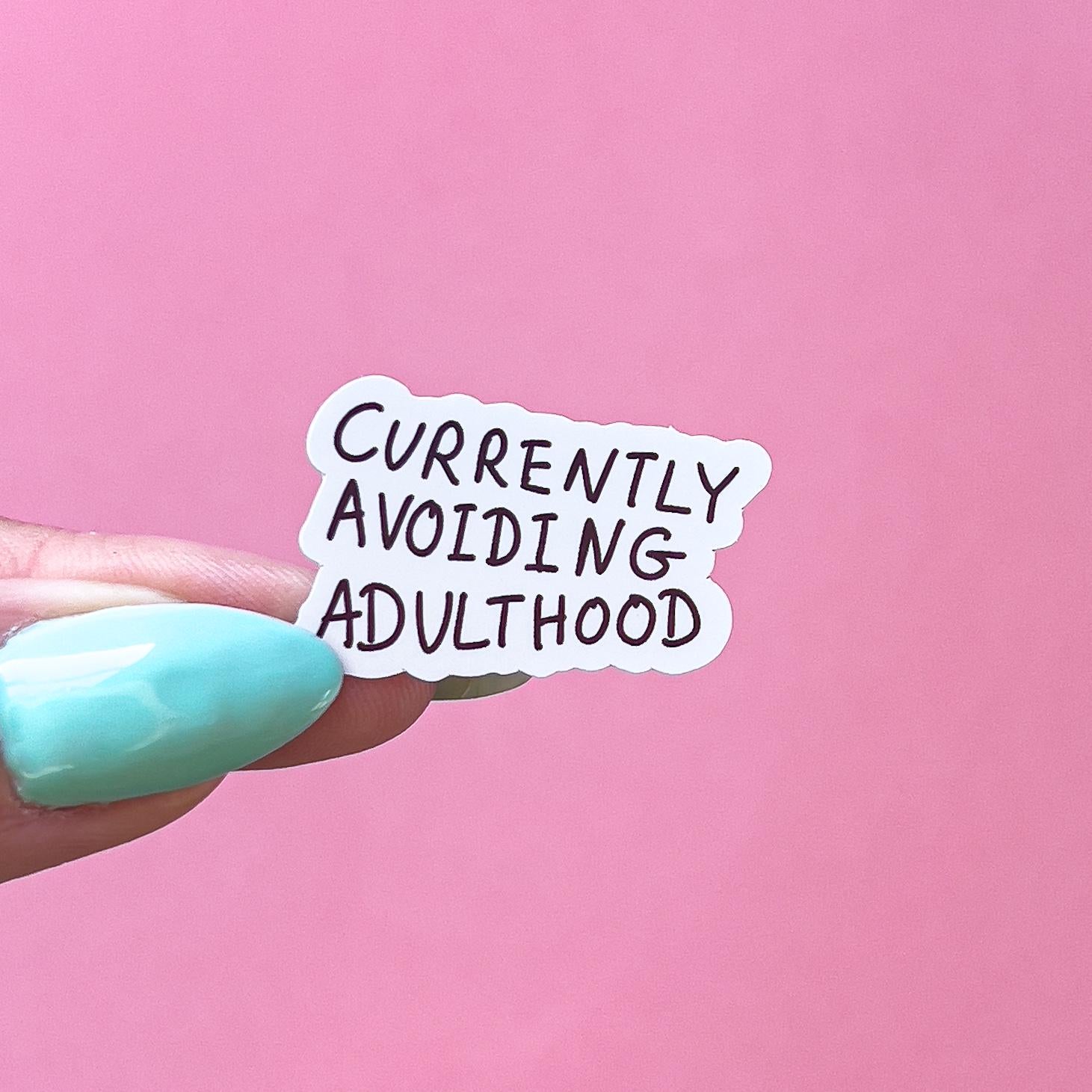 A vinyl decal sticker with black text that reads 'Currently Avoiding Adulthood'.