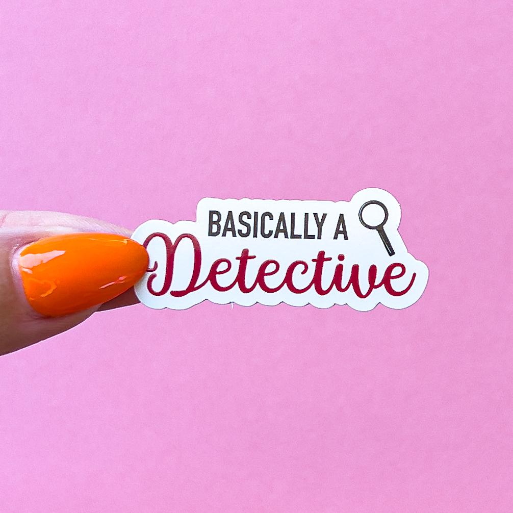 A vinyl decal sticker of black and read text that reads "Basically a detective" with a magnifying glass to the right side.
