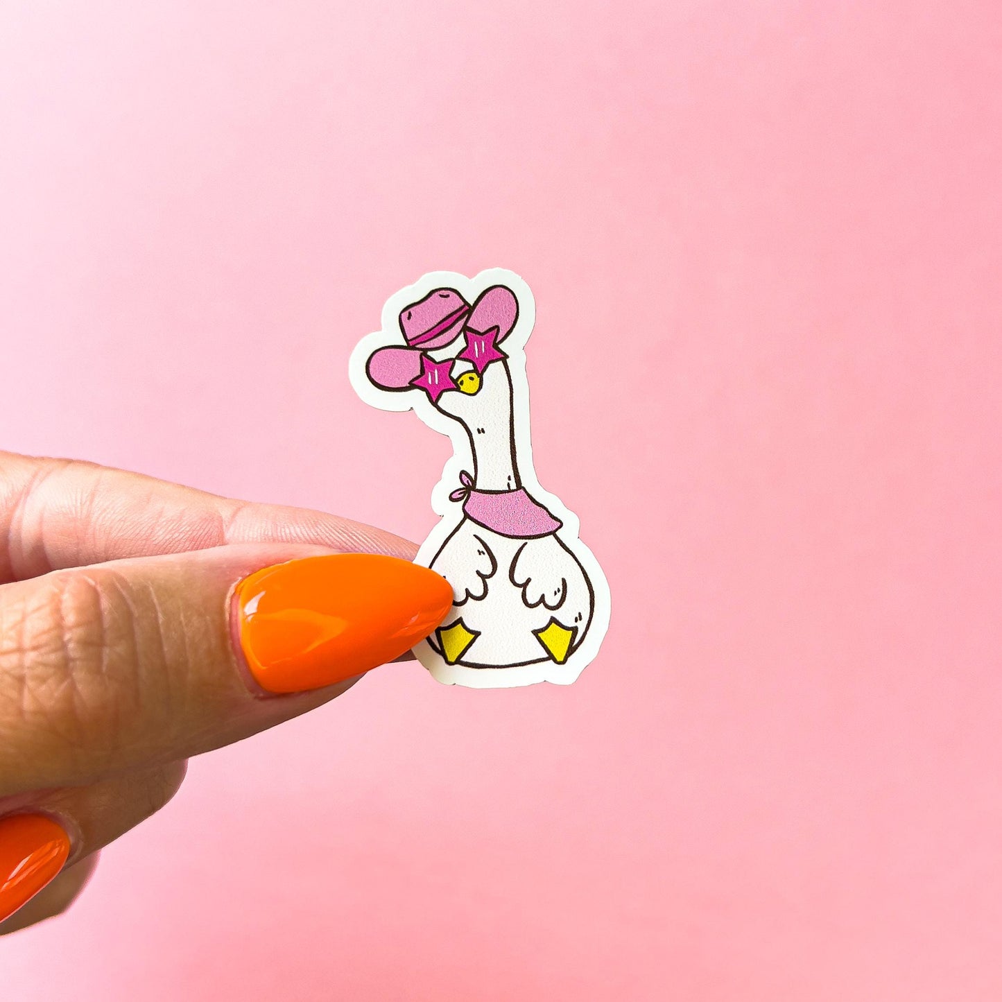 A vinyl decal sticker of a cowboy/western themed goose/duck. The goose/duck is wearing a pink cowboy hat, pink cowboy boots, pink star shaped glasses and a pink bandana around its neck. The goose/duck has a yellow beak and is sitting with its head tilted to the side and its feet out in front of it.