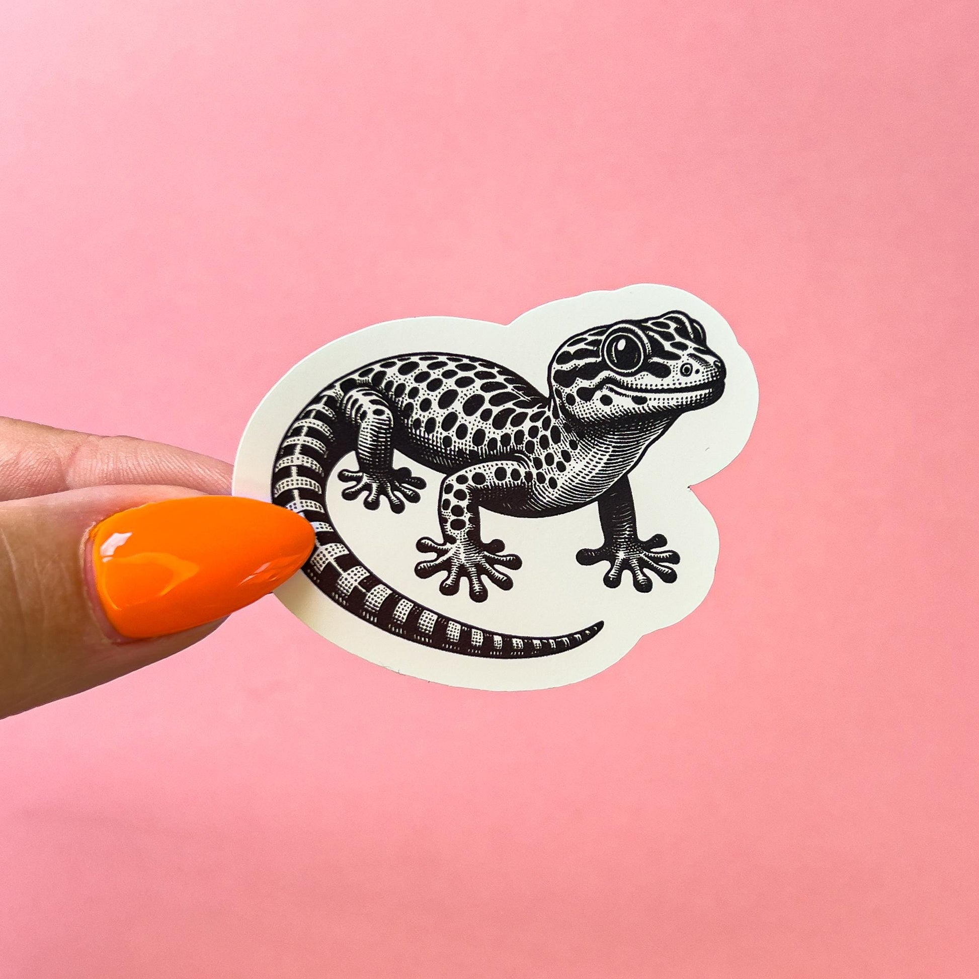 A vinyl sticker decal of a black and white leopard gecko. The gecko has a spotted pattern and is in a walking pose.