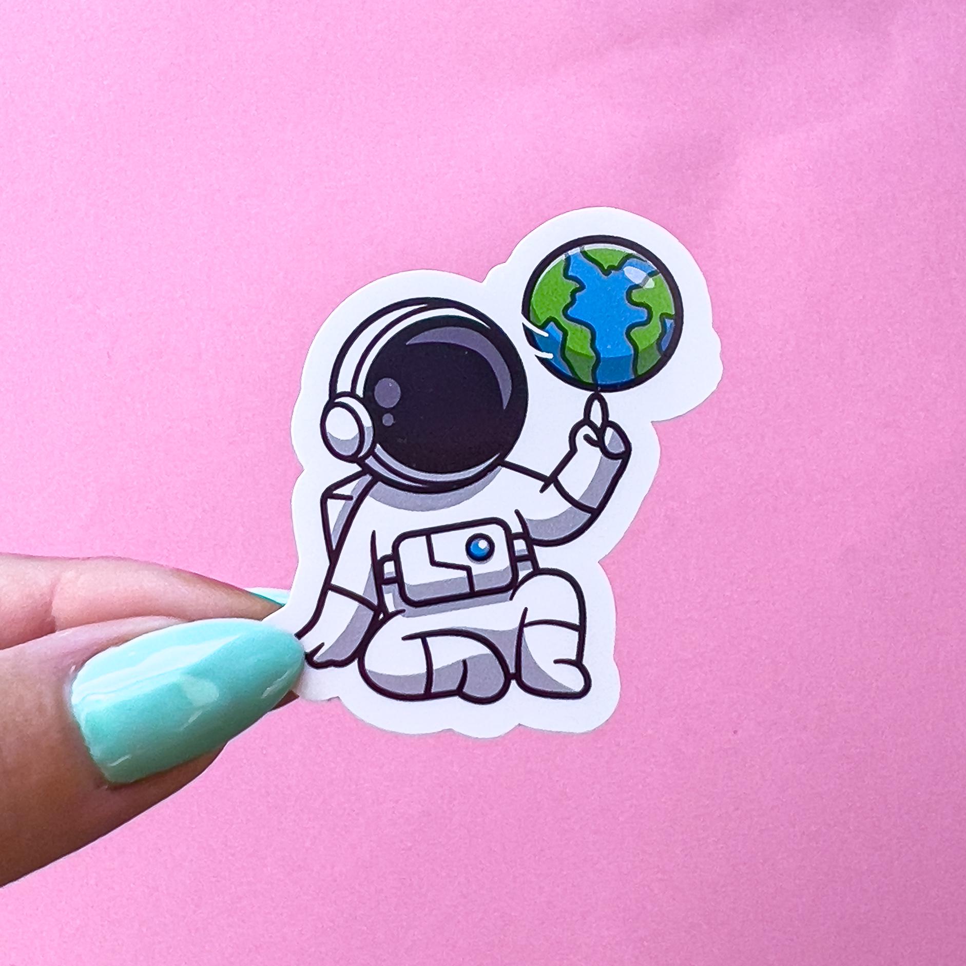 A vinyl decal sticker of an astronaut  sitting with one knee up and spinning the world on his finger.