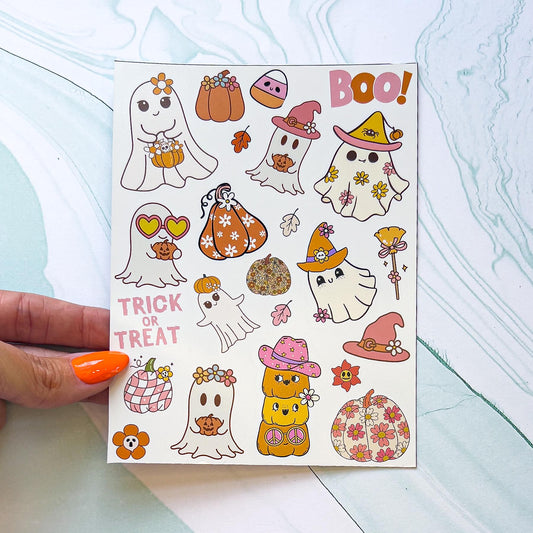 A Halloween vinyl decal sticker sheet featuring ghosts, pumpkins, leaves, a witches hat and broom, and a candy corn. Each sticker is retro themed, in various pink, white, beige, and orange colors. Many of the pumpkins and ghosts have flowers on them. There are two text stickers, one reads "BOO!" in pink and orange. The other reads "TRICK OR TREAT" in light pink.