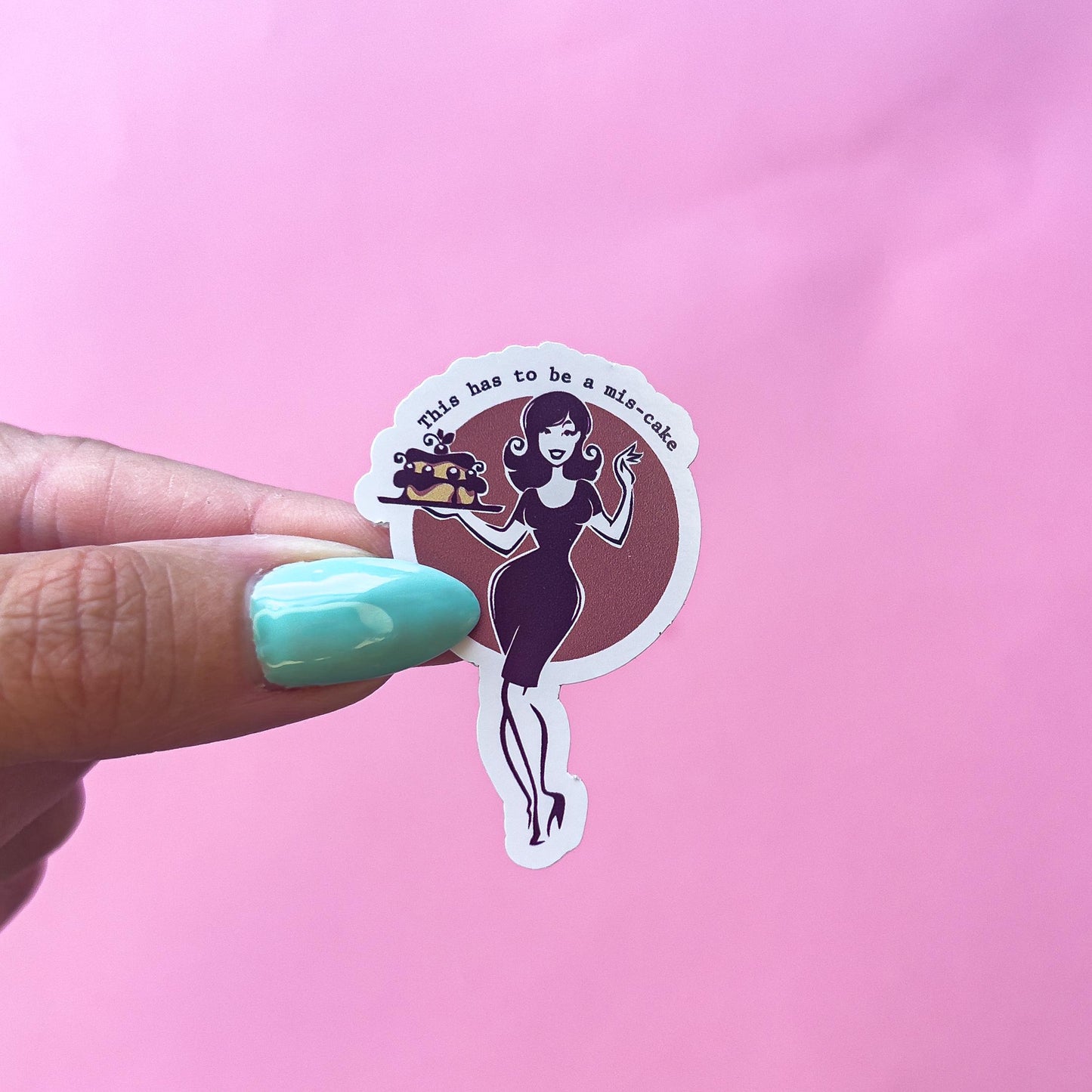 A sticker with a red background and a vintage style woman holding a cake and a drink. The text on the sticker reads 'This has to be a mis-cake.'
