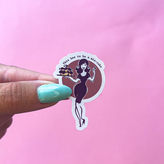 A sticker with a red background and a vintage style woman holding a cake and a drink. The text on the sticker reads 'This has to be a mis-cake.'
