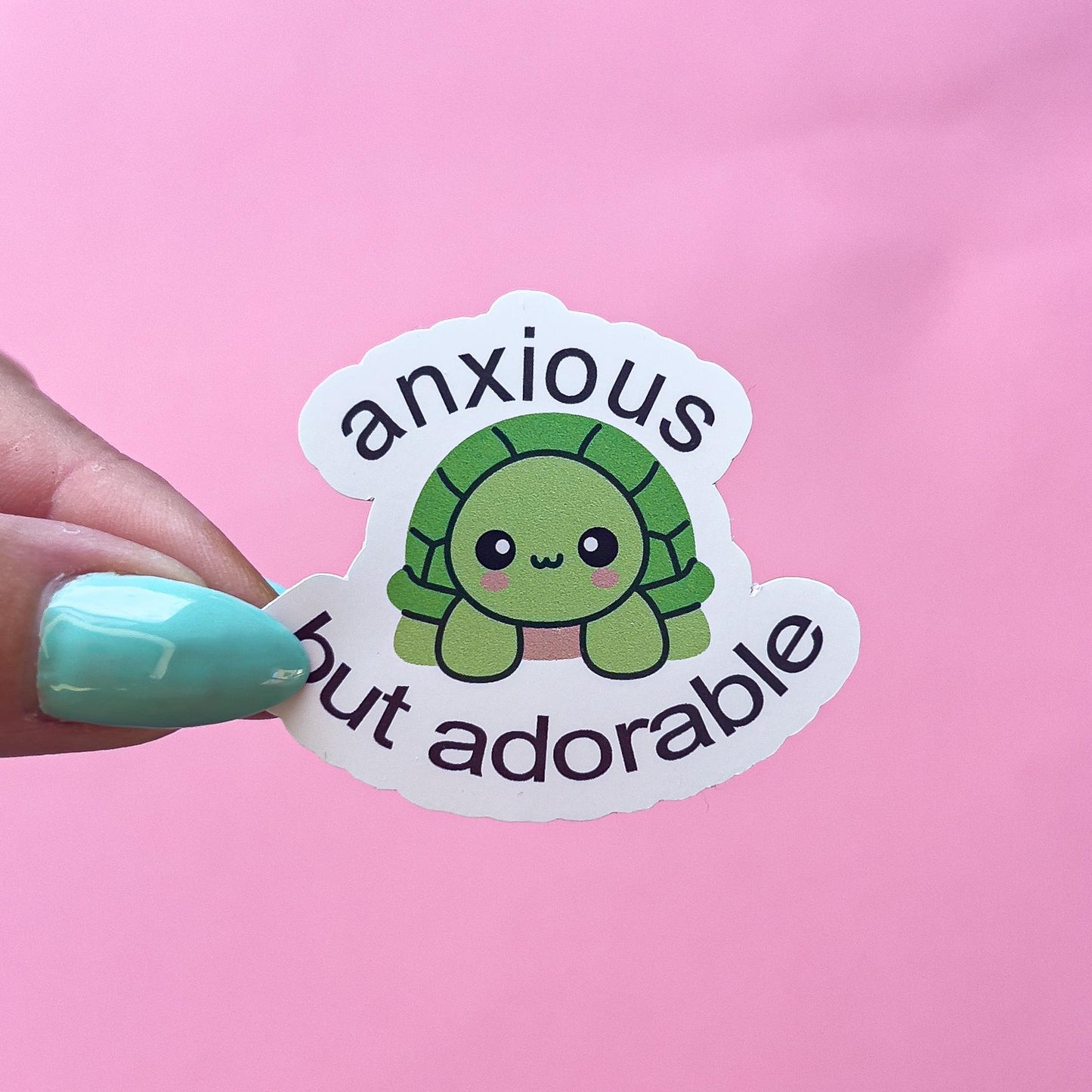 A vinyl decal sticker of a green cartoon kawaii turtle with the text 'anxious but adorable'. The turtle has pink blushed cheeks.