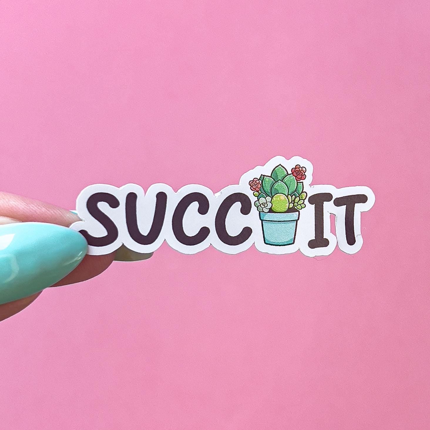 A vinyl decal sticker that reads "SUCC IT" in black text. In between the two words is a green, red, and blue green succulent plant in a light blue pot.
