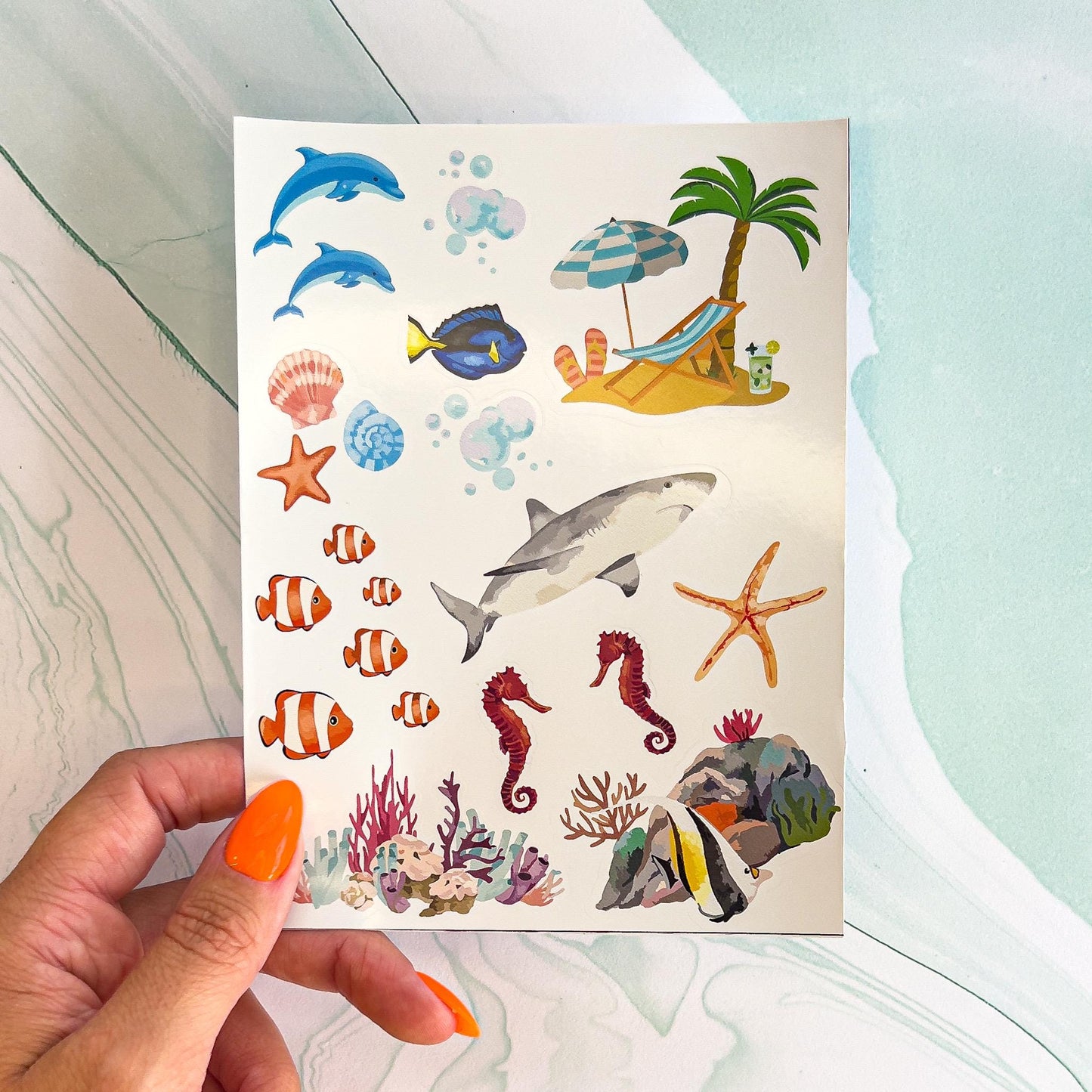 A set of colorful stickers featuring a variety of ocean-themed images, including dolphins, a shark, seahorses, starfish, coral, and a beach scene with a palm tree and a lounge chair.