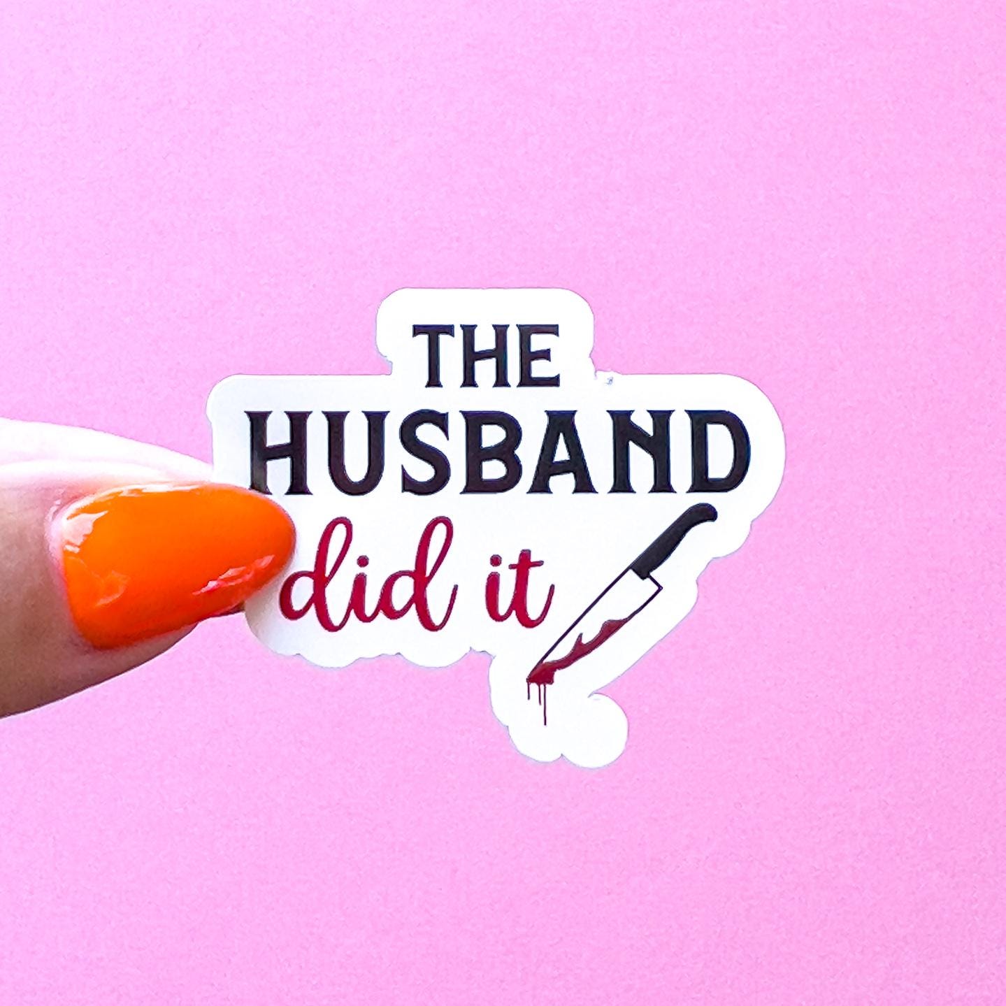 A vinyl decal sticker of black an d read text that reads "The husband did it" in stylized font and a knife to the right.