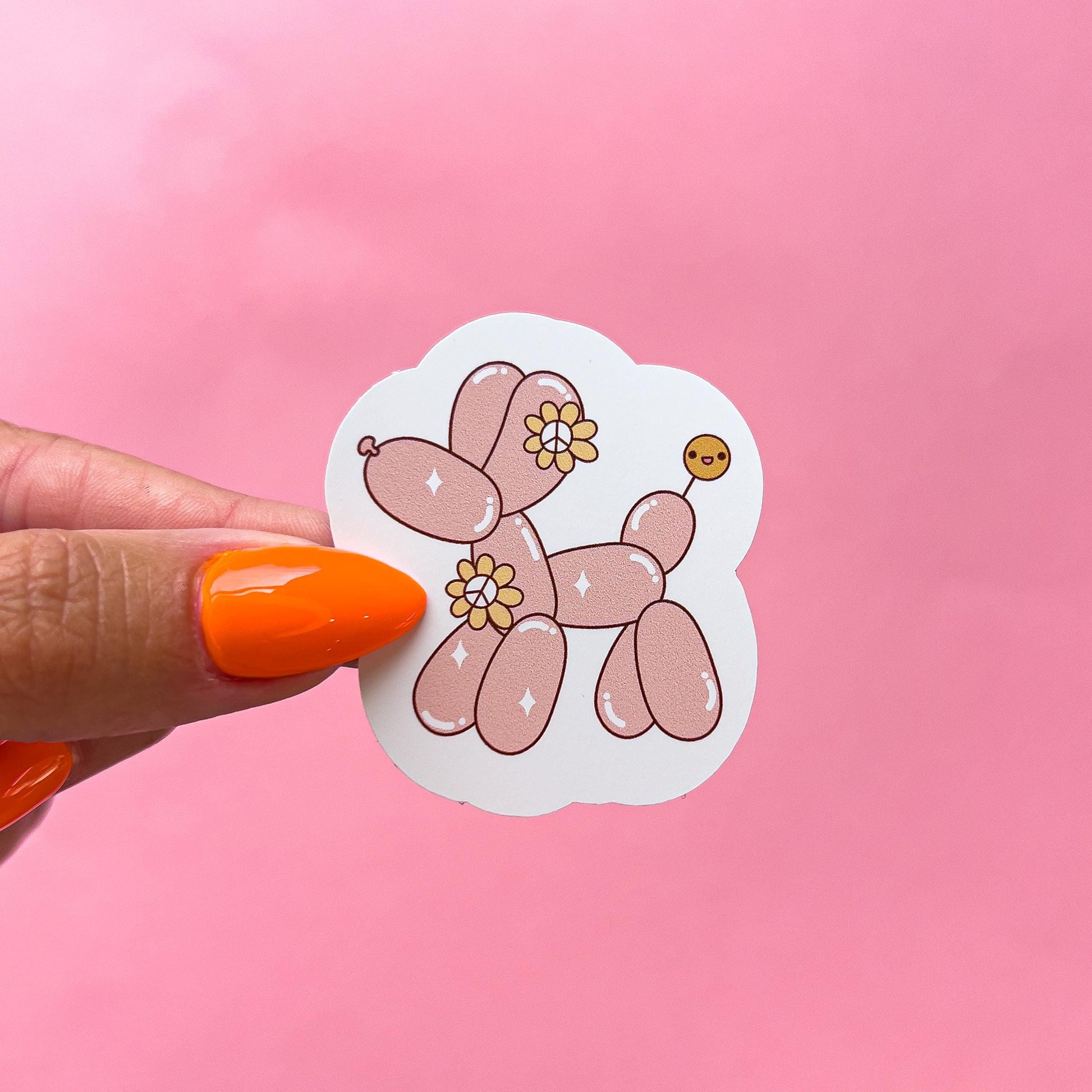 A pink balloon animal shaped like a dog with yellow flowers and glitter. The poodle has a small brown balloon tail with a smiley face.