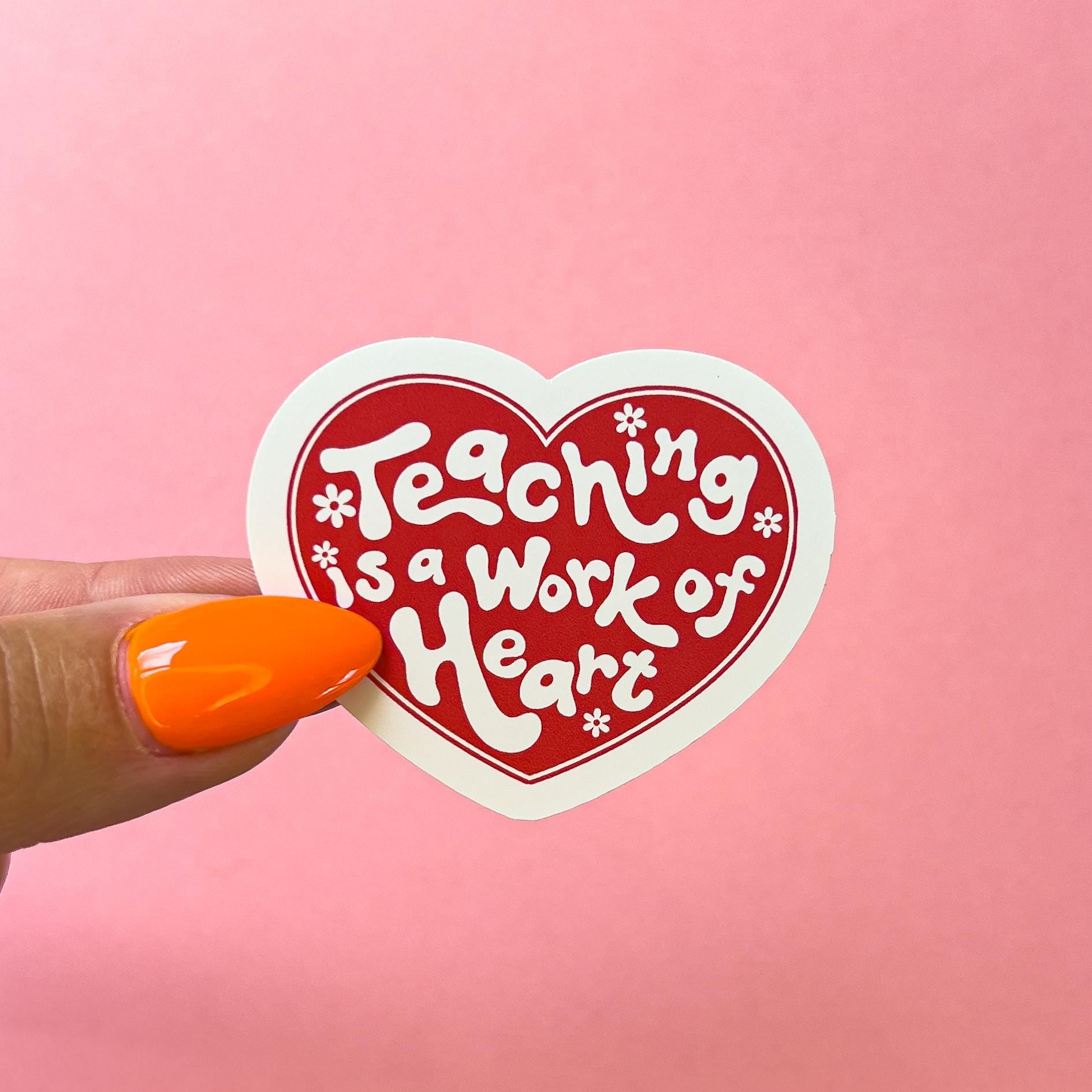 A vinyl decal sticker with white stylized text that reads 'Teaching is a Work of Heart' in a red heart.